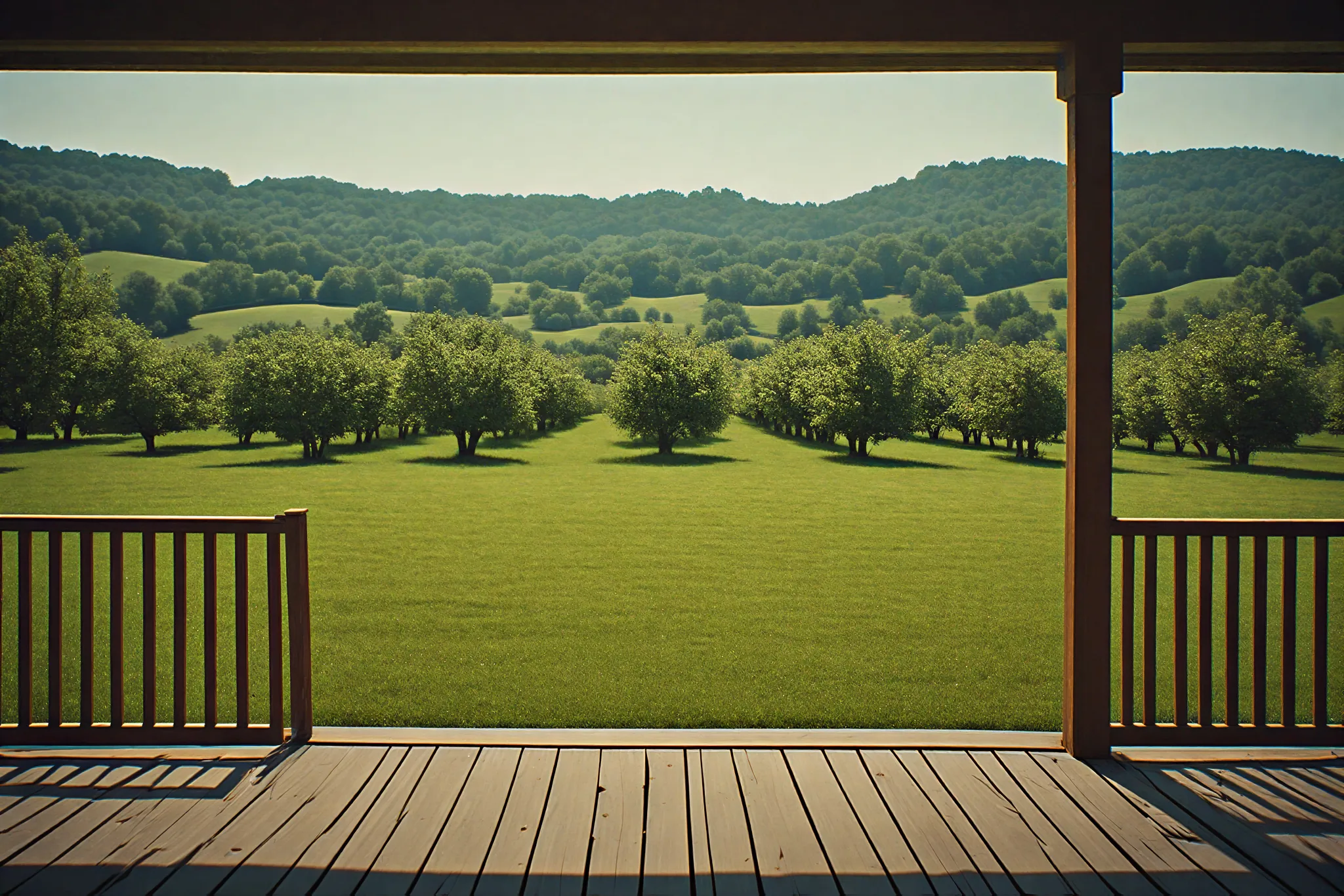 The view from the front porch of Orchard Lane House: wood floorboards and rail, rows of apple trees across a mown lawn, and wooded hills beyond.